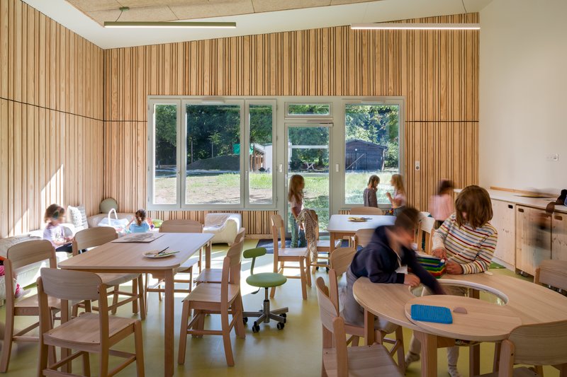 Classroom with striped timber wall panels and children seated at wooden tables on green flooring