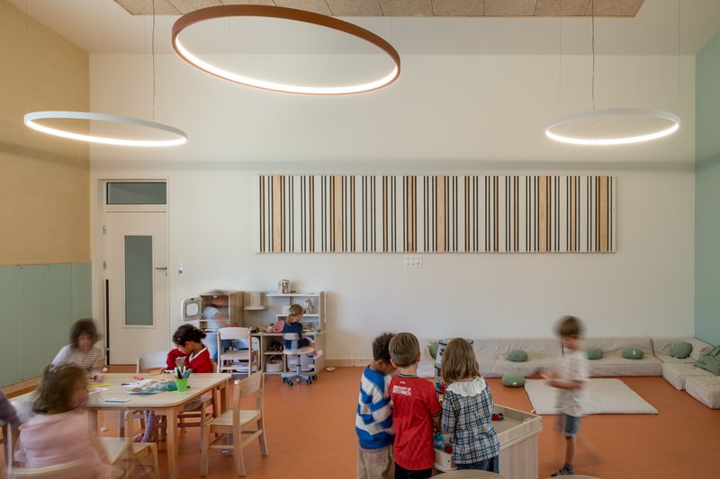 Classroom interior with circular ring pendant lights and children moving around orange linoleum floor