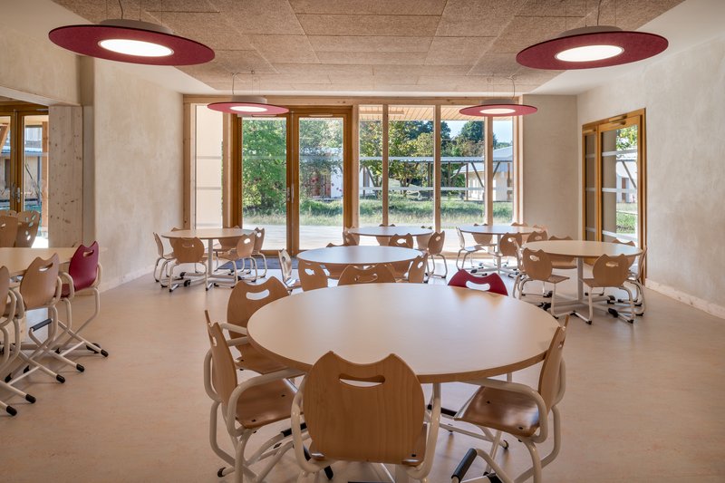 Classroom interior with round timber tables and large windows overlooking the courtyard garden in daylight
