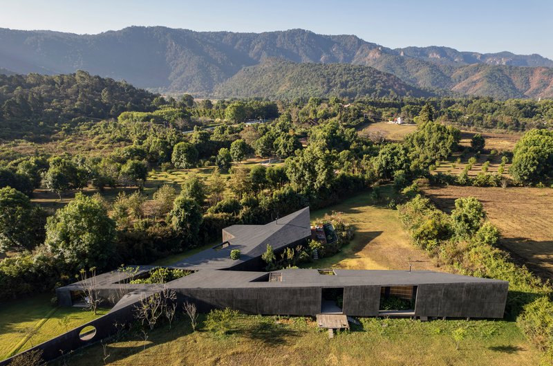 Aerial view of the angular concrete volumes set in a grassy clearing with forested hills beyond