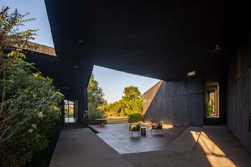 Covered terrace beneath angular concrete planes with scattered seating in late afternoon light