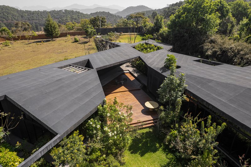 Drone view of clustered gabled roofs forming courtyards with planted beds and timber walkways linking the pavilions