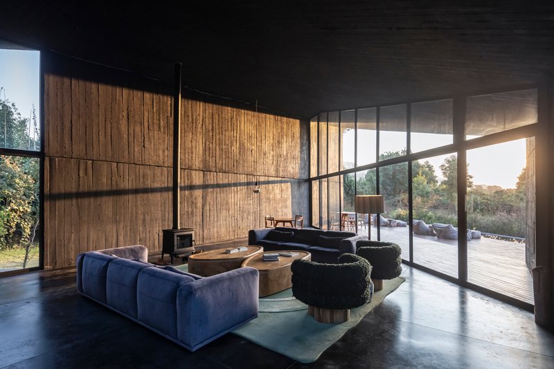 Interior living space with vertical timber wall panels and floor-to-ceiling glazing opening to timber deck at sunset