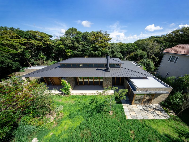 Aerial view of the low-slung metal roof volumes surrounded by lawn and forest canopy