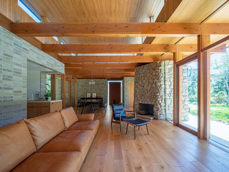 Living room with exposed timber beams, stone fireplace wall and full-height glazing opening to the lawn