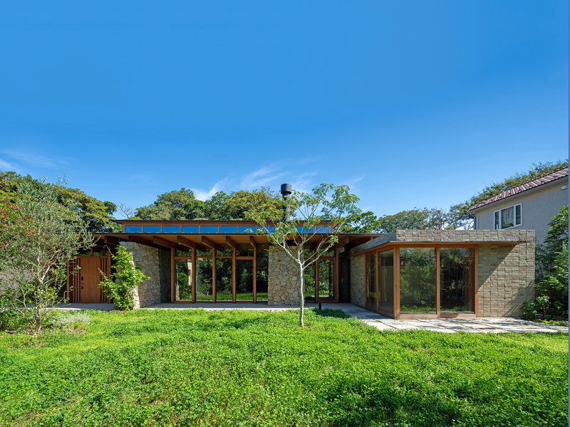 Garden elevation showing stone walls and timber-framed glazing under a flat roof on a sunny day