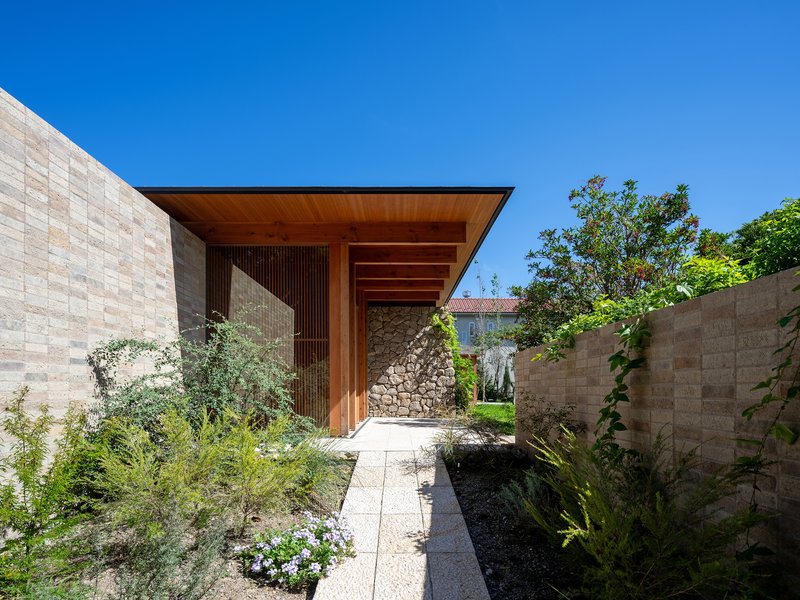 Entry courtyard with planted beds between stone block walls leading to a timber-clad entry portal