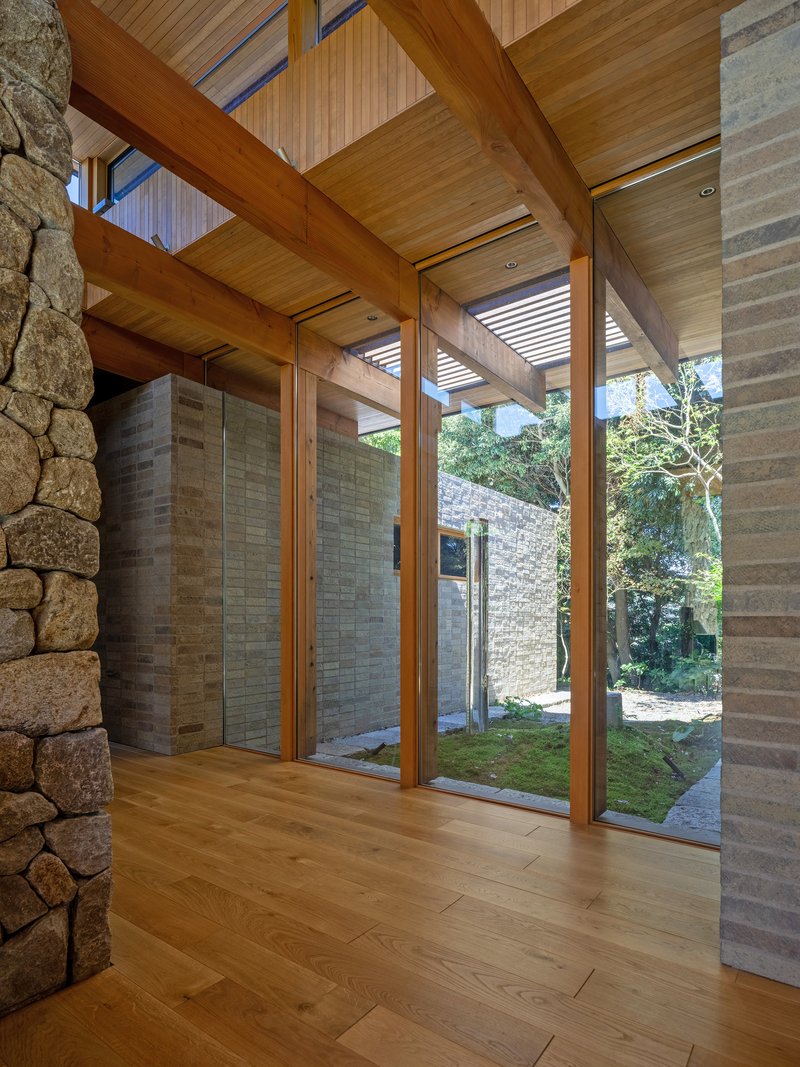 Floor-to-ceiling glazing between timber posts with fieldstone wall and courtyard beyond