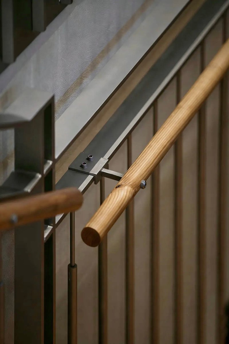 Timber handrail with steel bracket connecting to vertical slat balustrade beside a white ceiling plane