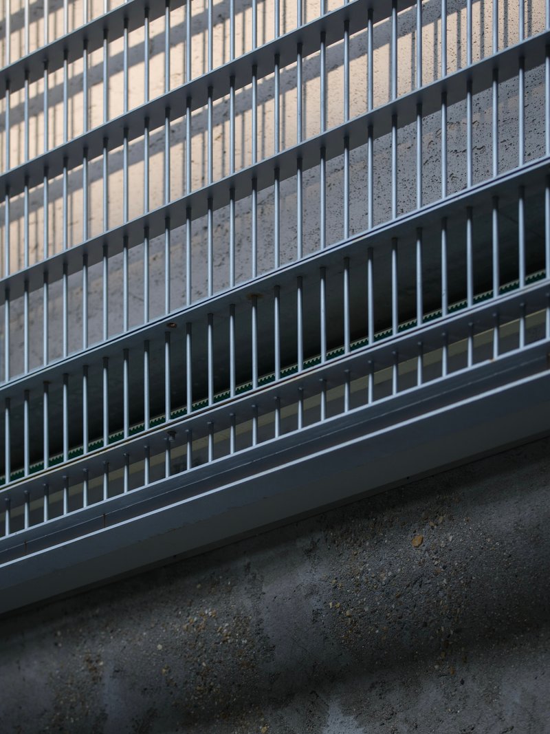 Detail of metal balustrade with vertical fins and horizontal rails meeting a concrete floor