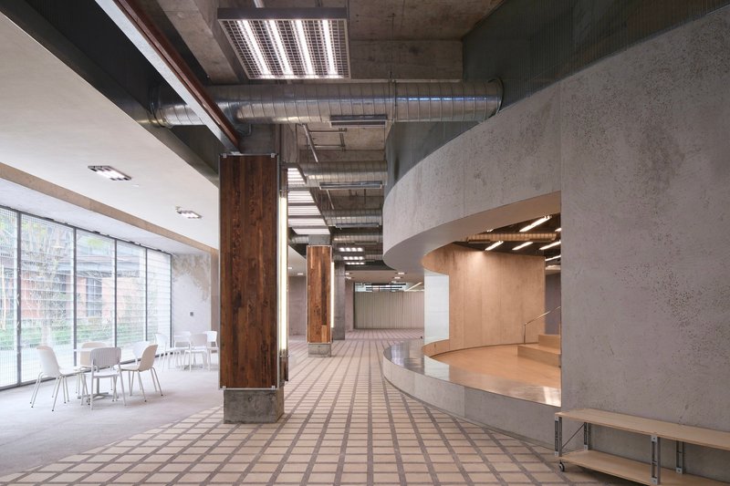 Interior hallway with timber-wrapped columns, exposed concrete ceiling, curved reception desk, and gridded floor tiles