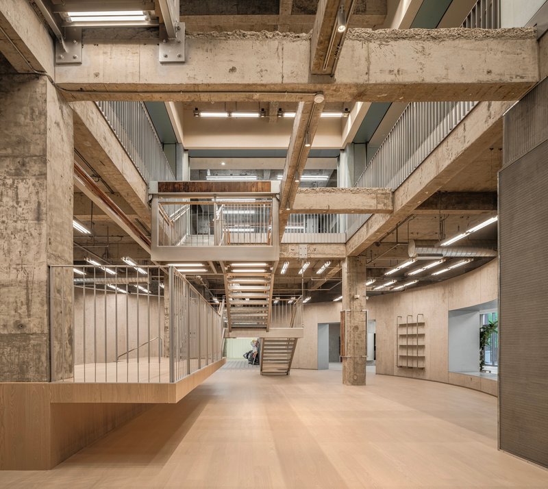 Multi-level atrium with exposed concrete beams, timber staircases, and vertical slat partitions wrapping openings
