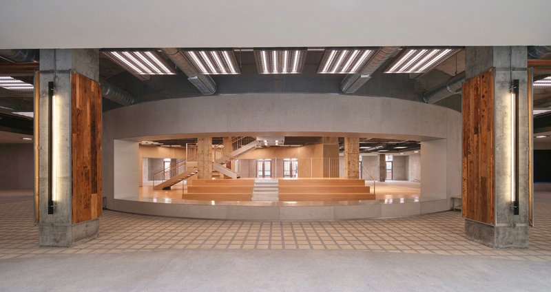 View through a curved opening into a timber-lined atrium with staircases and balconies under exposed beams