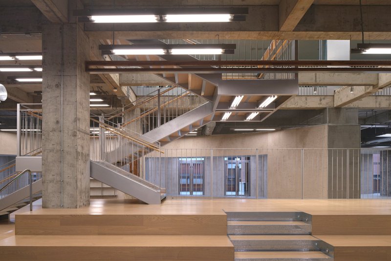 Intersecting metal staircases with vertical bar railings rising through the concrete and timber structural frame