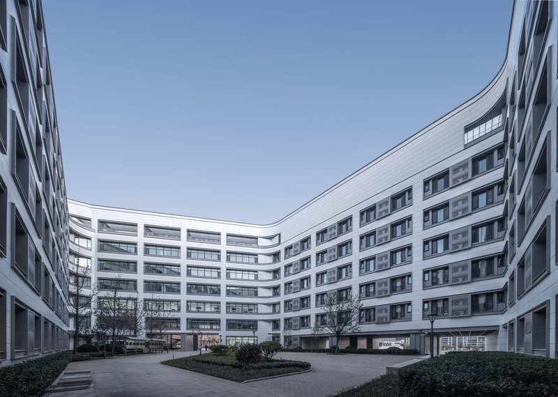 Interior courtyard enclosed by curved white facades with planted beds and bare trees under grey sky