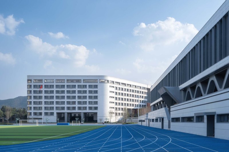 Campus view showing white residential towers and gymnasium with diagonal bracing beyond a blue running track