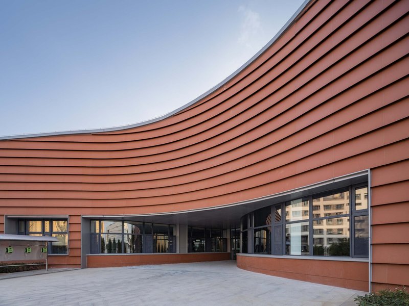 Courtyard view of the curved terracotta-clad facade with ribbon windows under a clear blue sky