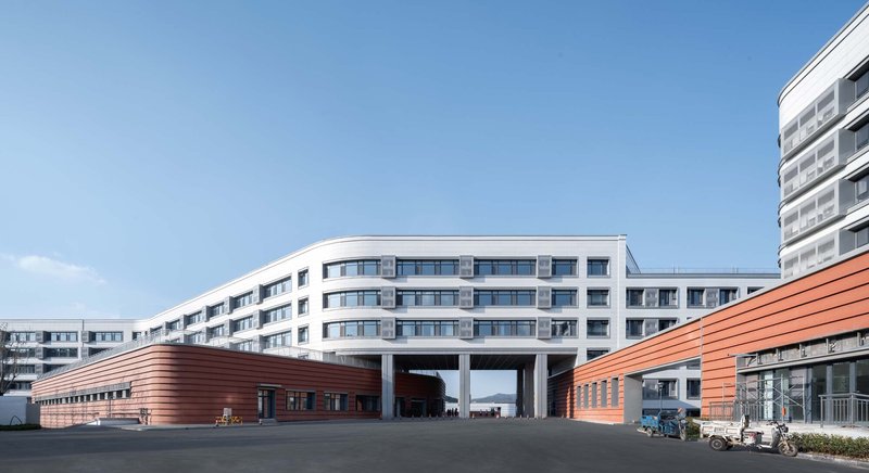 White concrete block elevated on columns over two red-clad horizontal volumes under clear blue sky