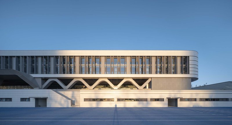 Curved white facade with zigzag structural supports illuminated by low evening sun