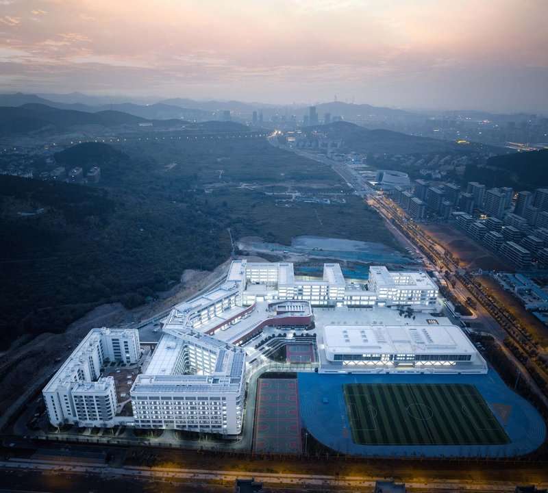Drone view of the illuminated campus at dusk with athletic fields and surrounding urban development