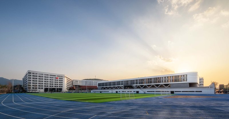Wide view of the campus showing running track, playing field, and residential and athletic buildings at sunset