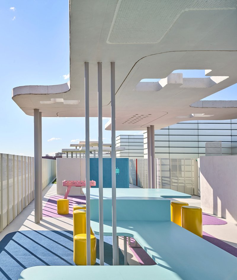View through cylindrical columns toward pool area with pink decking and mesh screens in bright sun
