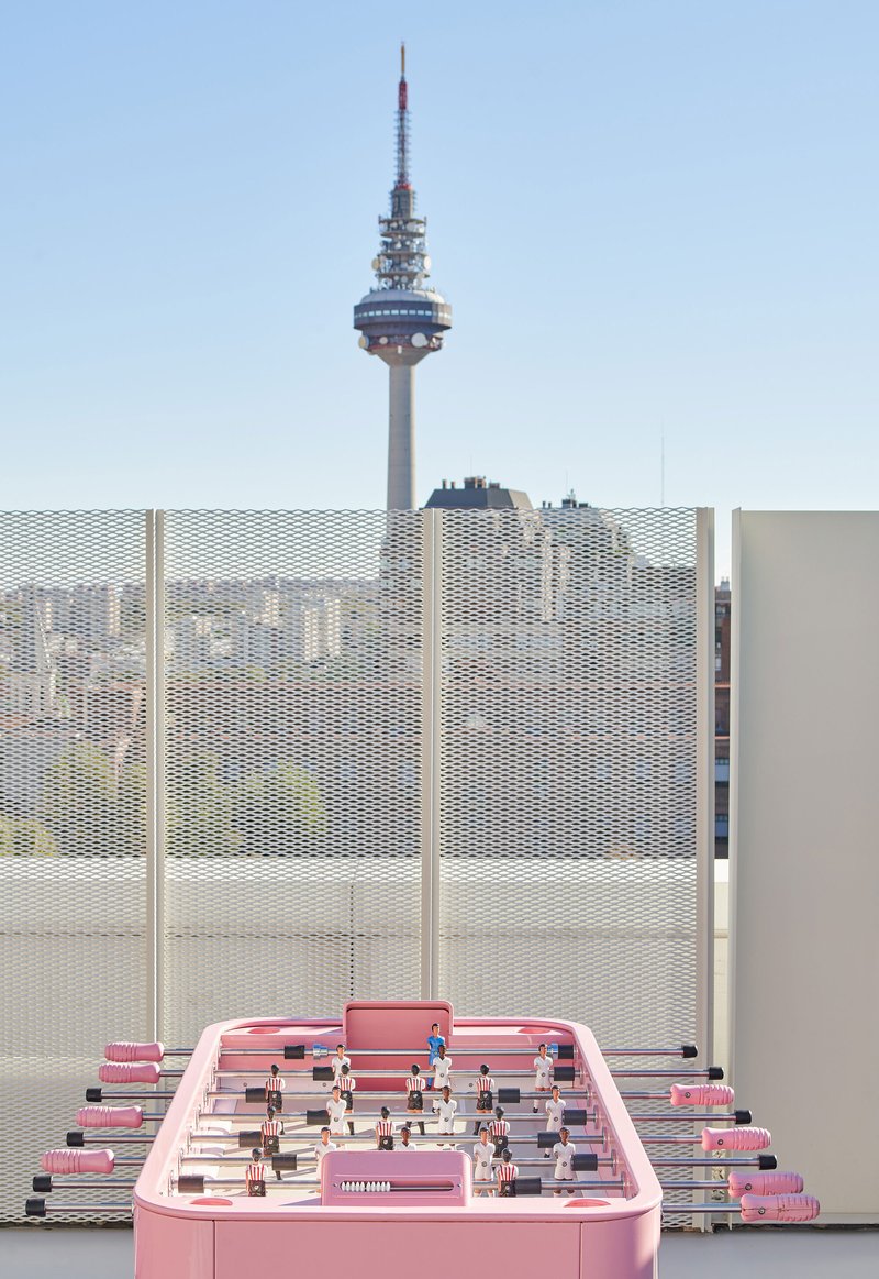 Pink foosball table on rooftop with perforated metal screens and telecommunications tower in distance