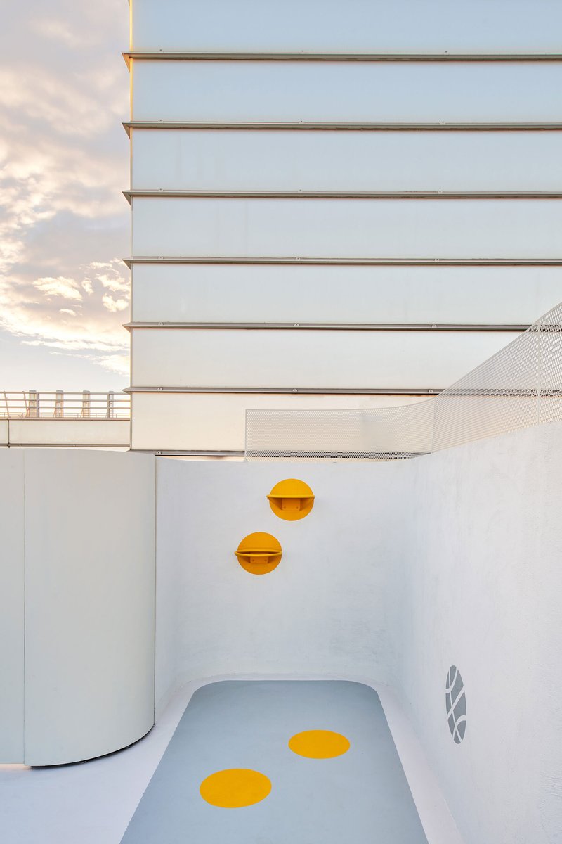 White play slide with yellow circular accents beside horizontal metal cladding at dusk