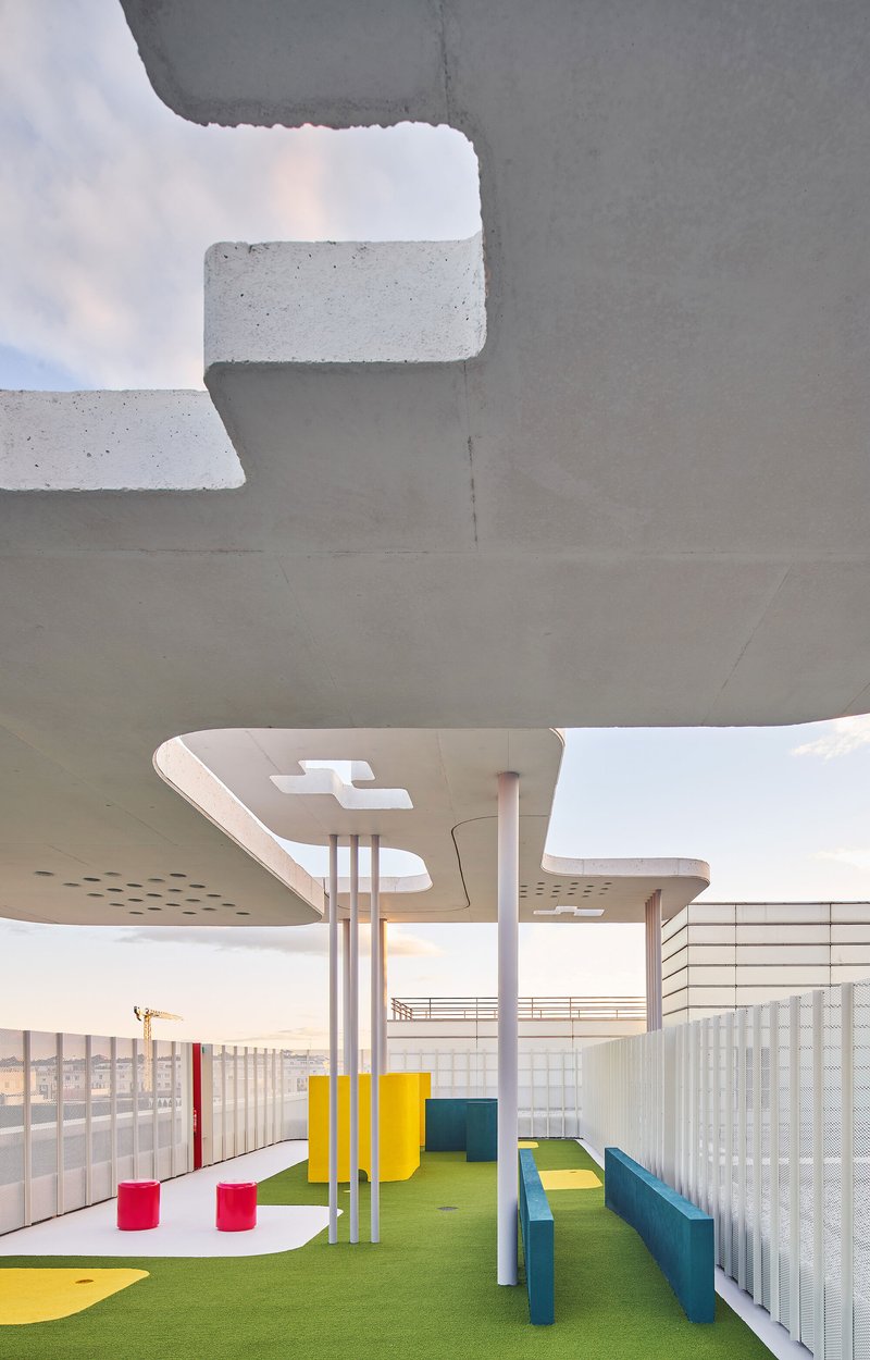 Underside of concrete canopy with perforations and cylindrical supports over artificial turf play area