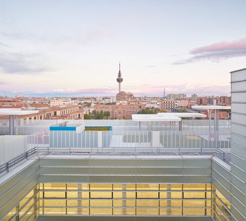 Rooftop courtyard with translucent glass panels and colorful accents overlooking the urban skyline at dusk