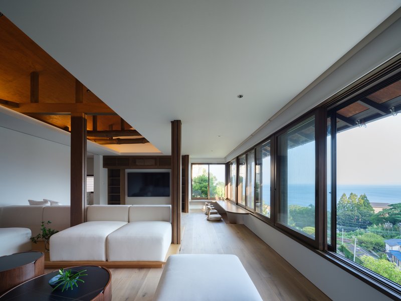 Continuous glazed wall opening to coastal landscape with low seating platform and recessed timber ceiling above