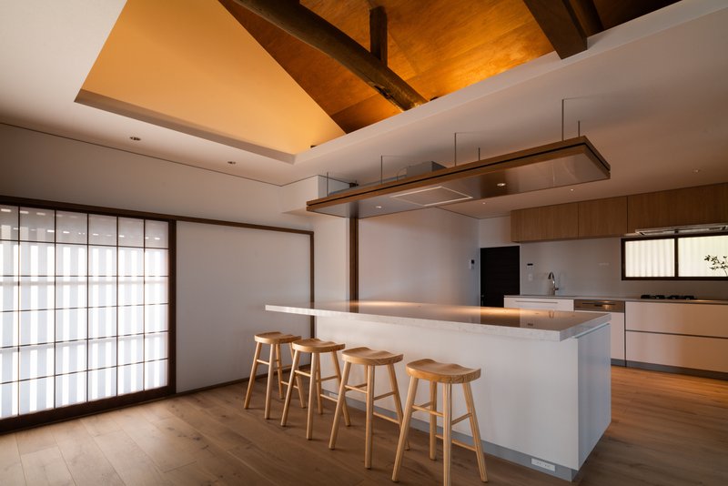 Kitchen island with three timber stools beneath a recessed timber ceiling and translucent sliding screen