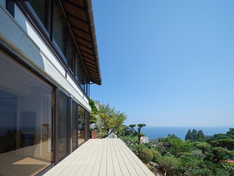 Timber deck terrace with full-height glazing and deep overhanging eaves overlooking a garden and ocean