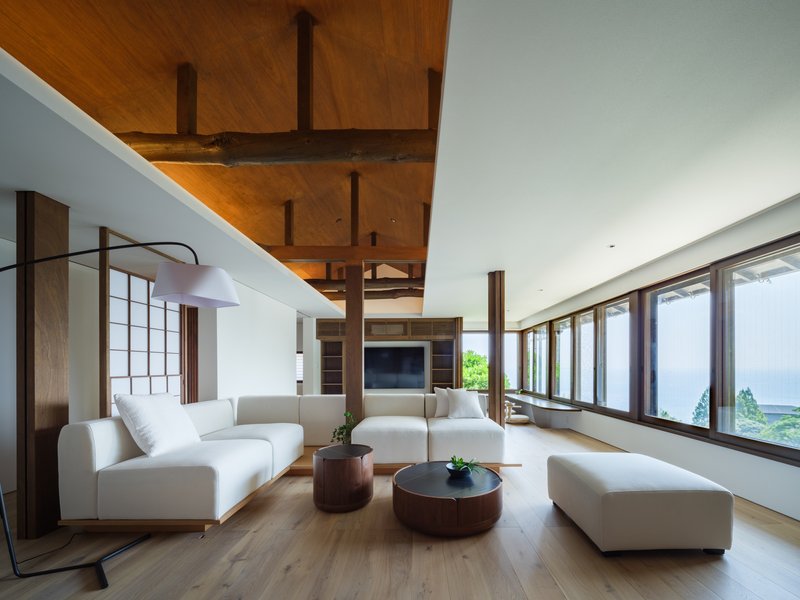 Living room with exposed timber ceiling beams and horizontal window band framing a distant ocean view