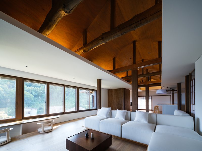 Interior showing the angular timber ceiling with recessed lighting above white seating and wood flooring