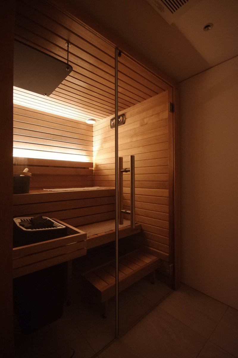 Wood-lined sauna with horizontal slat benches and glass door under warm recessed lighting