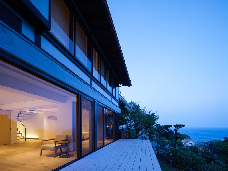 Timber deck terrace with sliding glass doors opening to interior under blue twilight sky and ocean