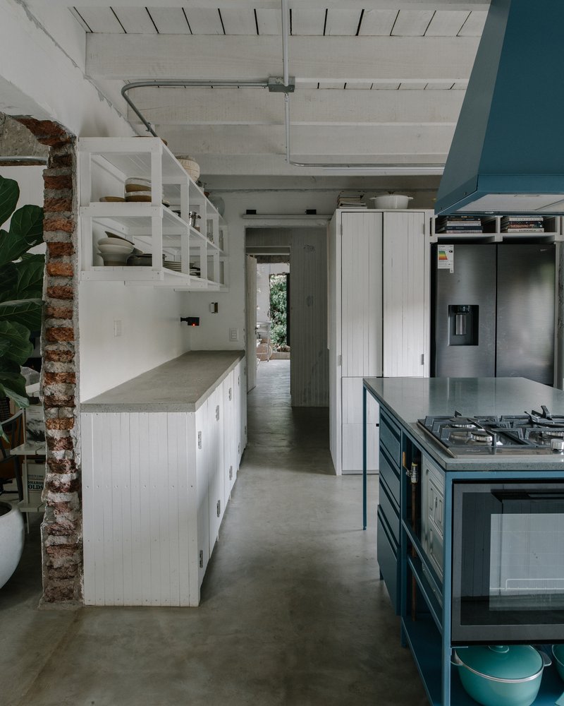 Kitchen interior with white cabinetry, blue island, exposed brick column, and concrete ceiling with skylights