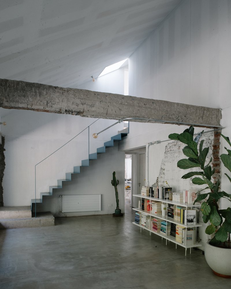 Double-height interior with blue metal staircase, exposed concrete beam, and slanted skylight above