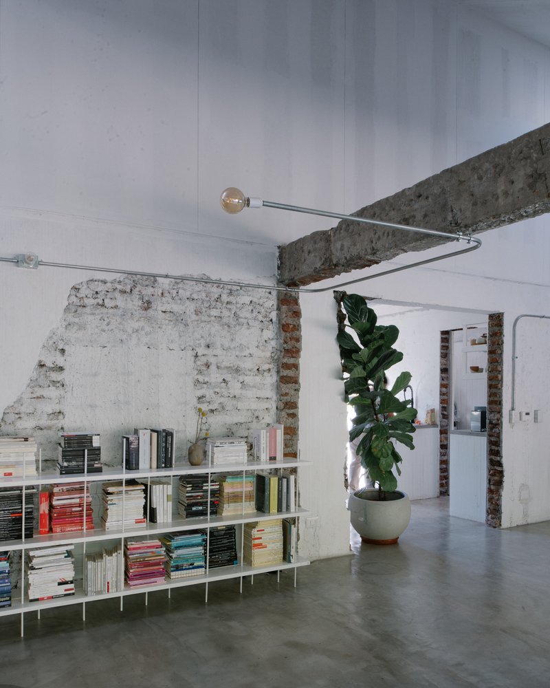 Looking up at exposed concrete beam with pendant light fixture and whitewashed brick partition below