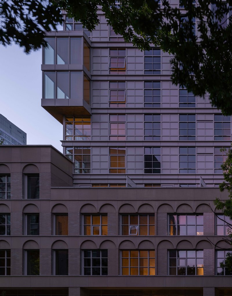 Tower facade rising above a renovated brick structure with arched openings at twilight