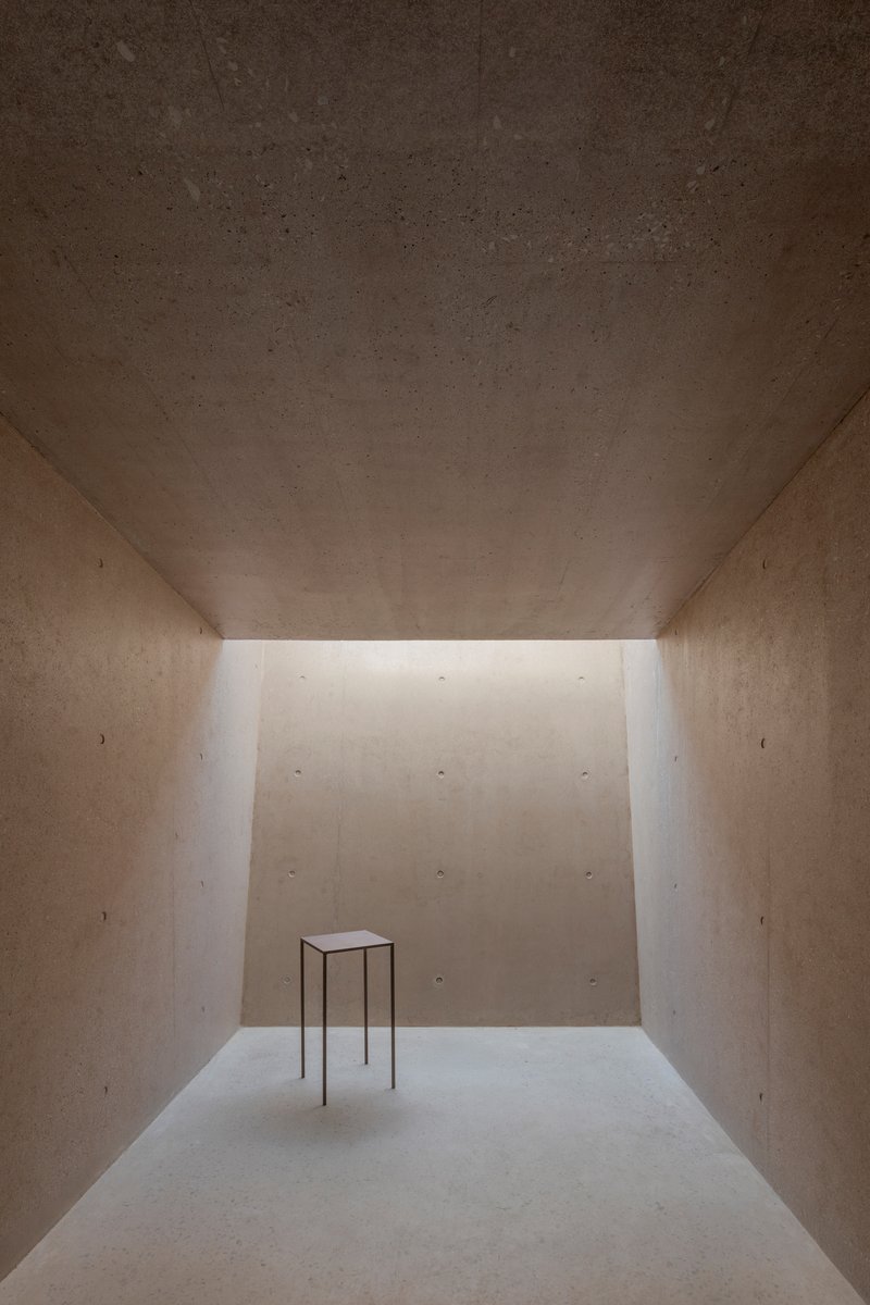Interior gallery space with clerestory lighting and solitary metal table on pale floor