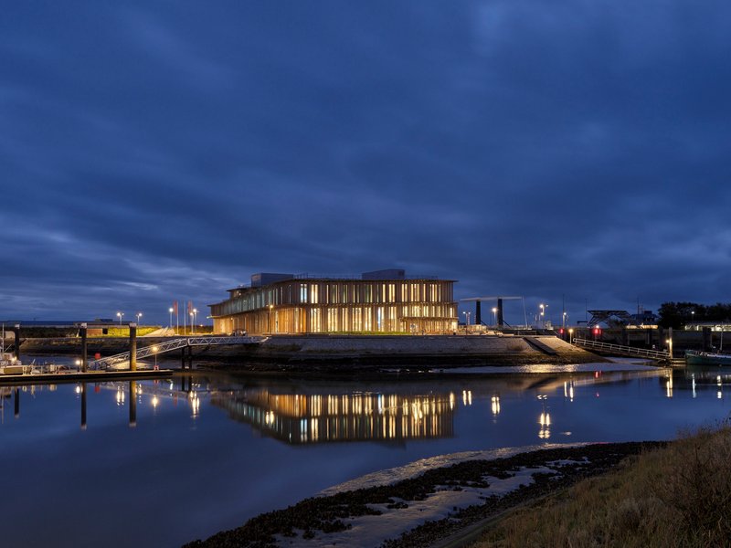 Illuminated building reflecting in calm tidal waters under evening sky with clouds