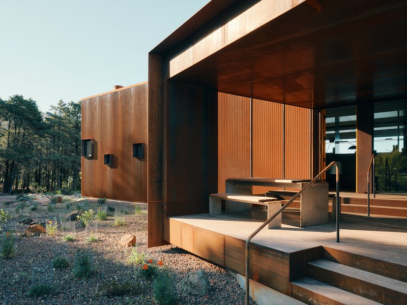 Concrete entry steps with weathered steel walls and vertical timber cladding at late afternoon