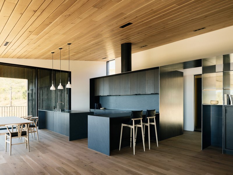 Open-plan kitchen and dining area with dark cabinetry, timber-slat ceiling and pendant lights