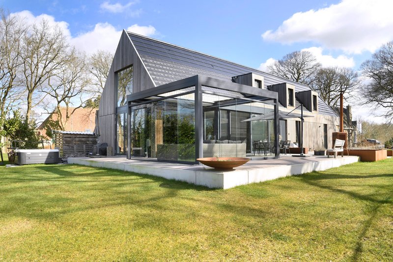Glazed pavilion extension with steel framing opening onto a concrete terrace and lawn