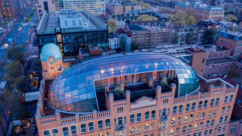 Aerial view of the curved glass roof structure atop a brick building at dusk