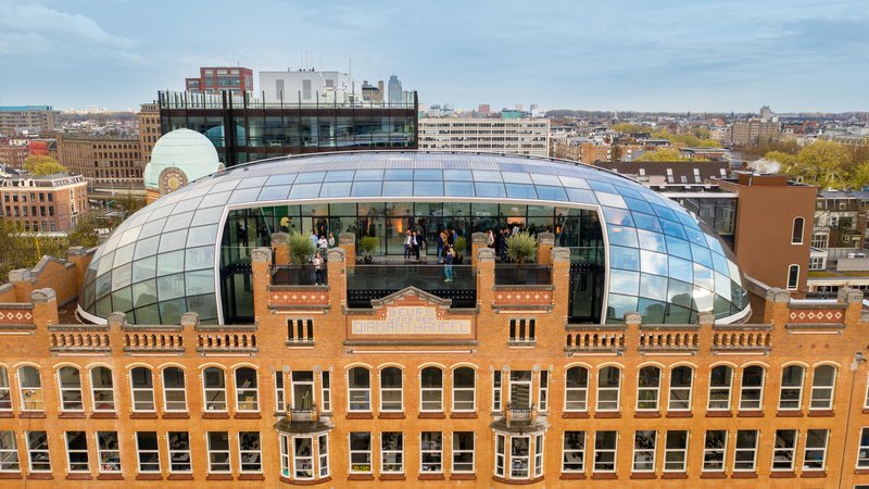 Barrel-vaulted glass canopy over a historic brick facade with visible occupants inside