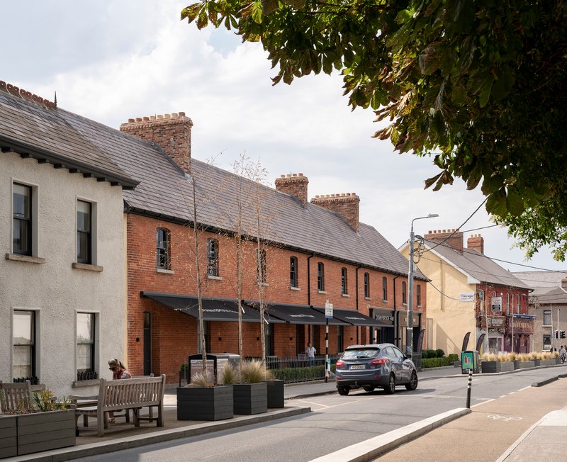 Street view of red brick terraced housing with slate roofs and planters along the sidewalk