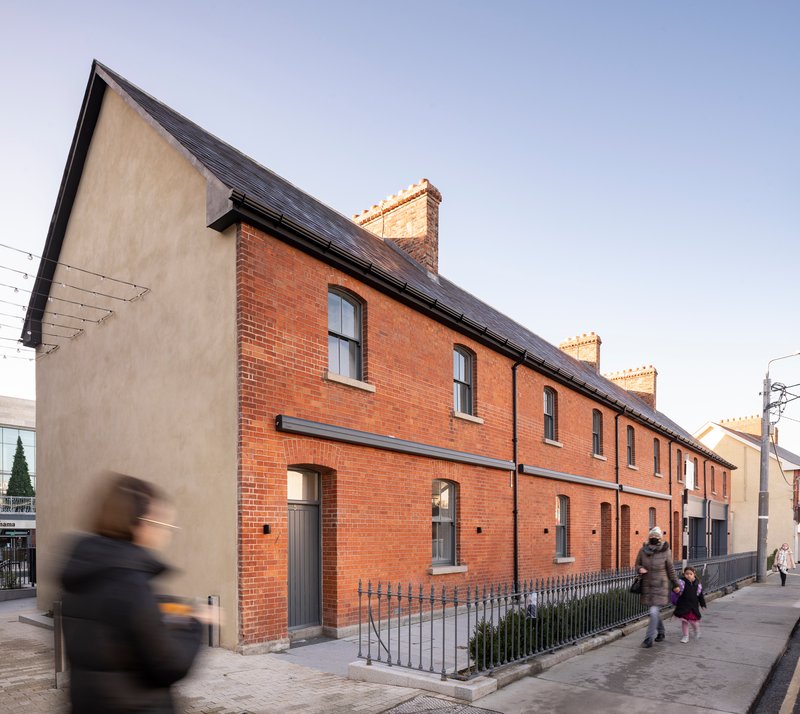 Corner of red brick row houses with slate roof and pedestrians passing on the pavement